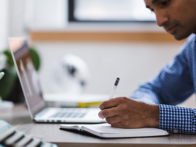 Man with laptop writing in journal